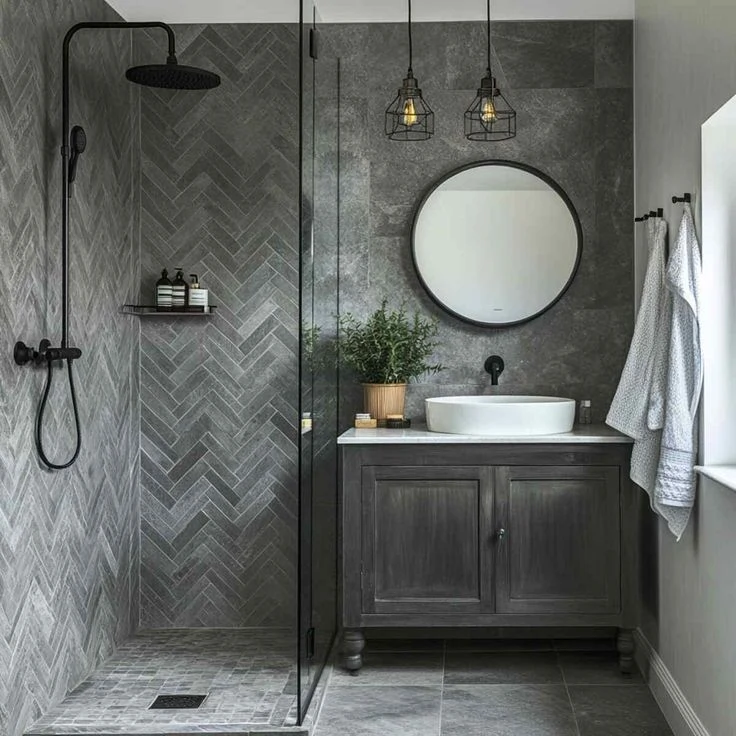 Dark gray herringbone tile shower wall with black fixtures in a moody bathroom
